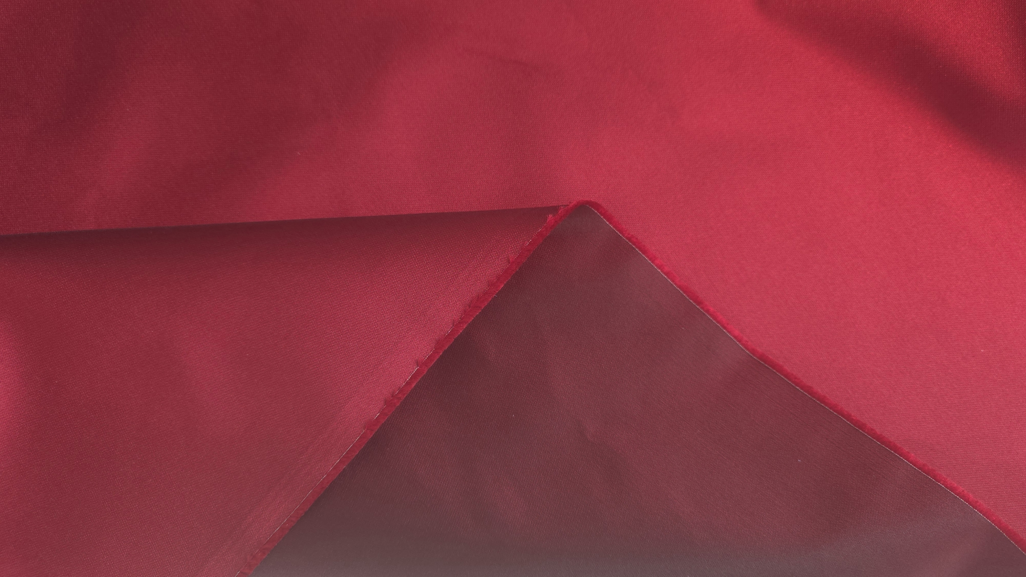 Material vișiniu pliat geometric, contrast între fața lucioasă și versoul mat