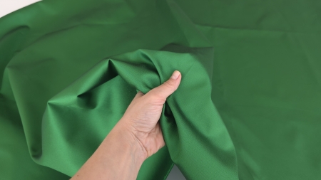Mână strânge material verde bogat, falduri neregulate dense și corp ferm vizibil
