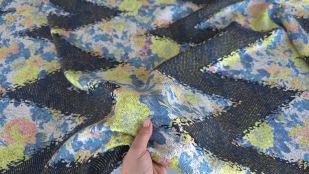 Material cu flori verde acid și albastre ridicat în mână, formând valuri peste benzile negre
