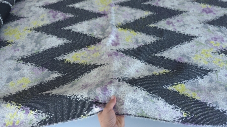 Țesătură cu zigzag negru și fond gri deschis cu flori mov, ținută în mână