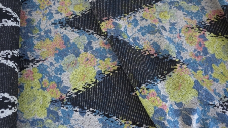 Țesătură pliată în straturi oblice, cu flori colorate și benzi negre, lângă un sul rulat