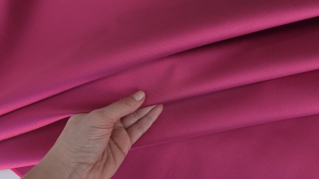 Mână care prinde ușor materialul magenta falduri paralele cu luciu perlat
