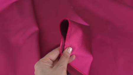 Mână care ține colțul materialului dos închis bordo vizibil la margine