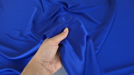 Satin albastru cobalt din matase naturala ridicat in mana peste falduri lucioase
