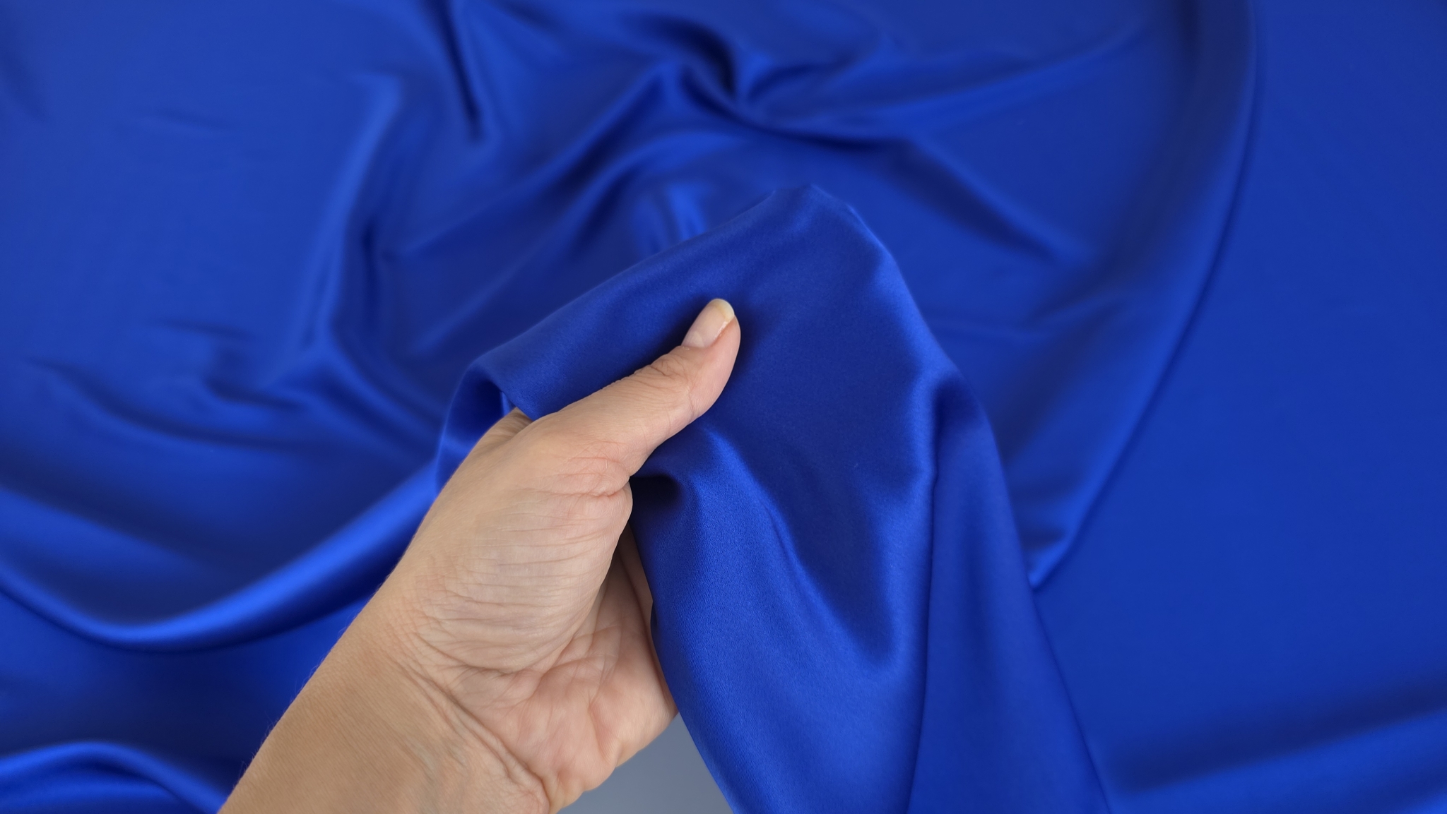 Satin albastru cobalt din matase naturala ridicat in mana peste falduri lucioase