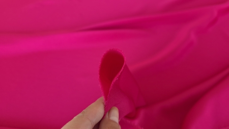 Crep satinat fucsia din fibre naturale MRN1168 cu margine de crep satinat fucsia prinsă între degete, cu grosime medie vizibilă