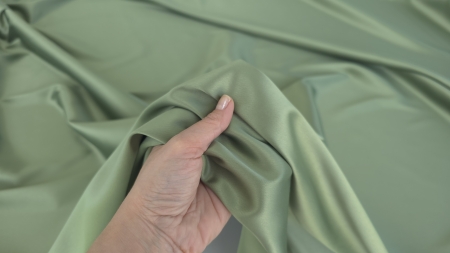 Mână ridicând material verde olive cu falduri naturale formate în jurul degetelor