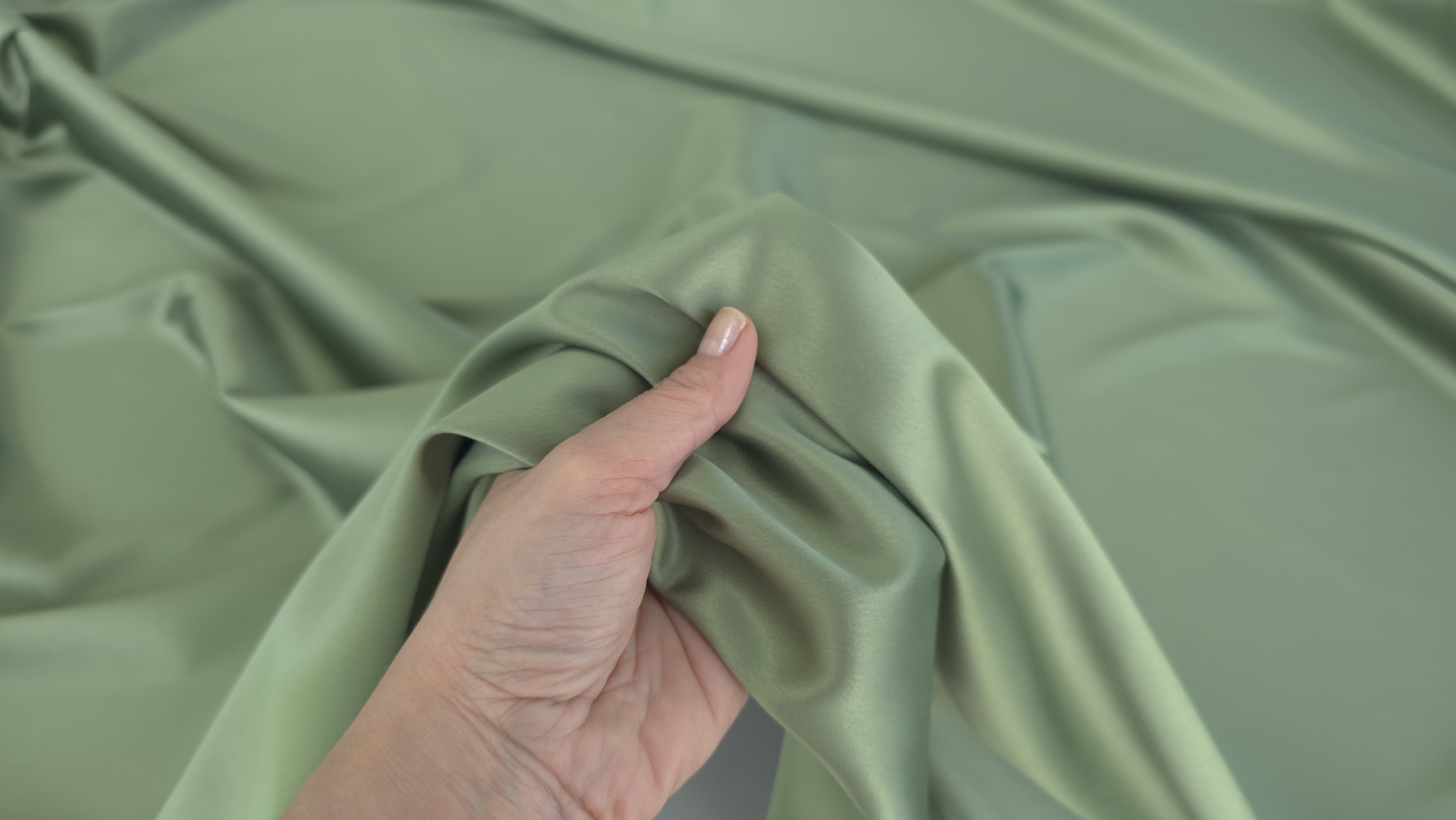 Mână ridicând material verde olive cu falduri naturale formate în jurul degetelor