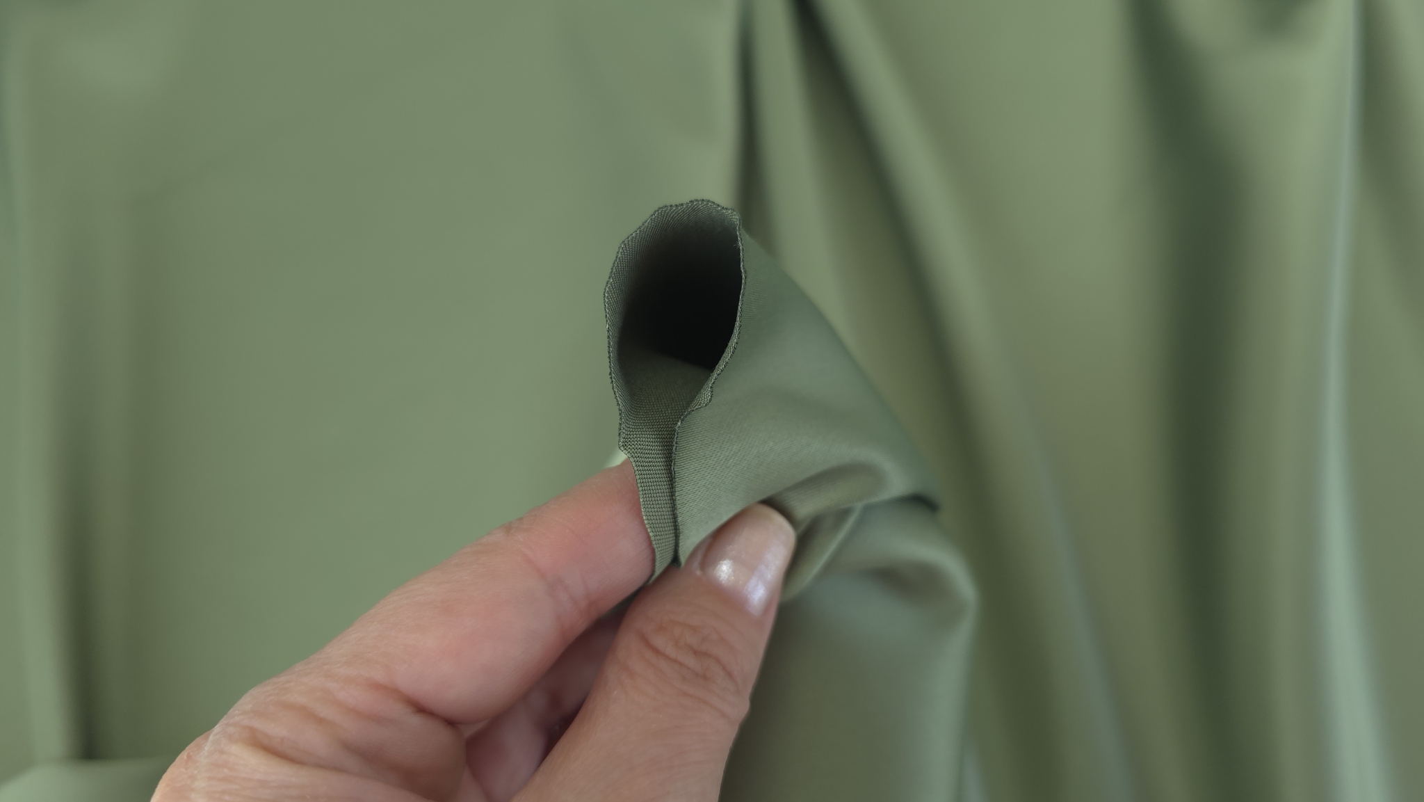 Mână ținând o buclă de tafta verde maslin 32037 răsucită cu marginea franjurată vizibilă