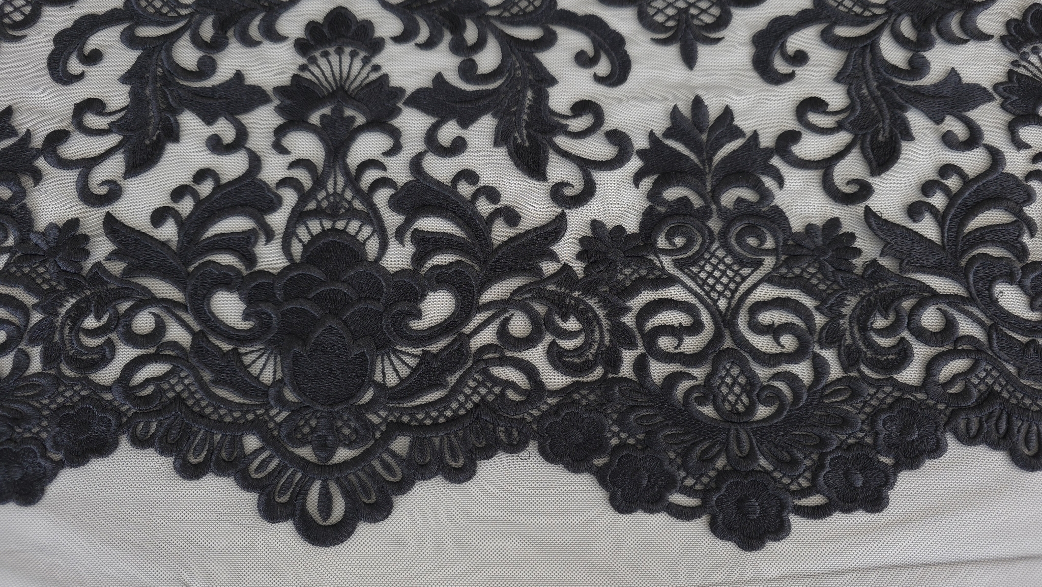 Broderie densă neagră pe tulle secțiune cu frunze stilizate, volute și bordură festonată cu flori, fără mână în cadru