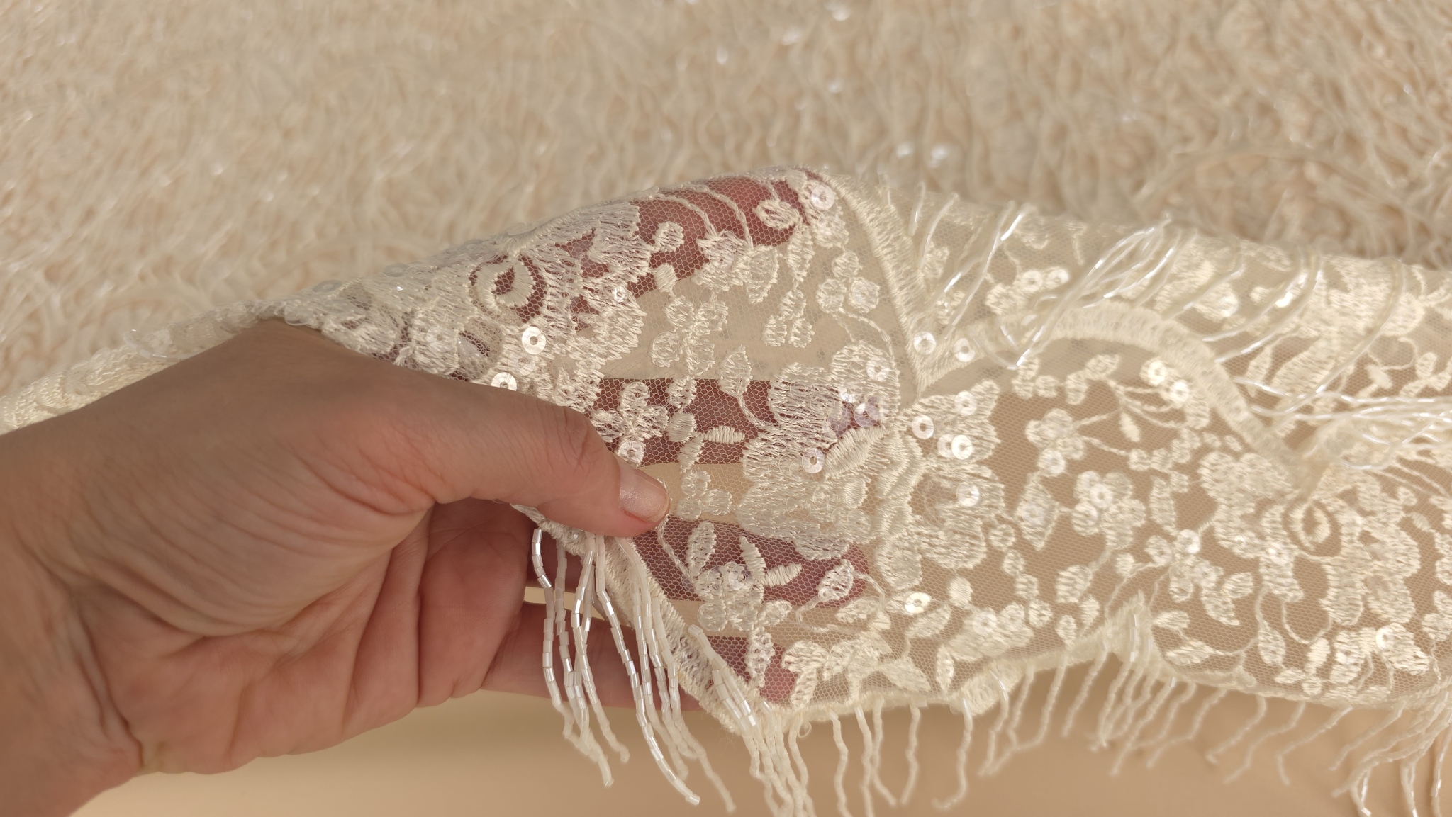 Colț de dantelă brodată cu micropaiete strălucitoare ținut în mână evidențiind franjurii de mărgele