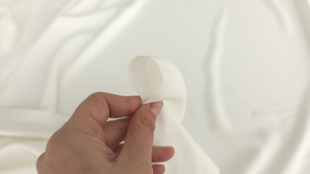 Colț de material ivoire ținut între degete, grosime medie vizibilă