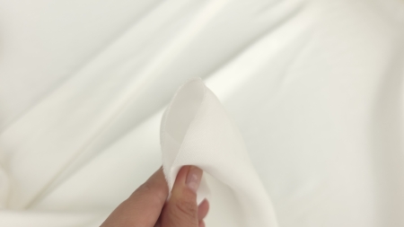 Colț de satin ivory din vâscoză ținut între degete, suprafață netedă vizibilă