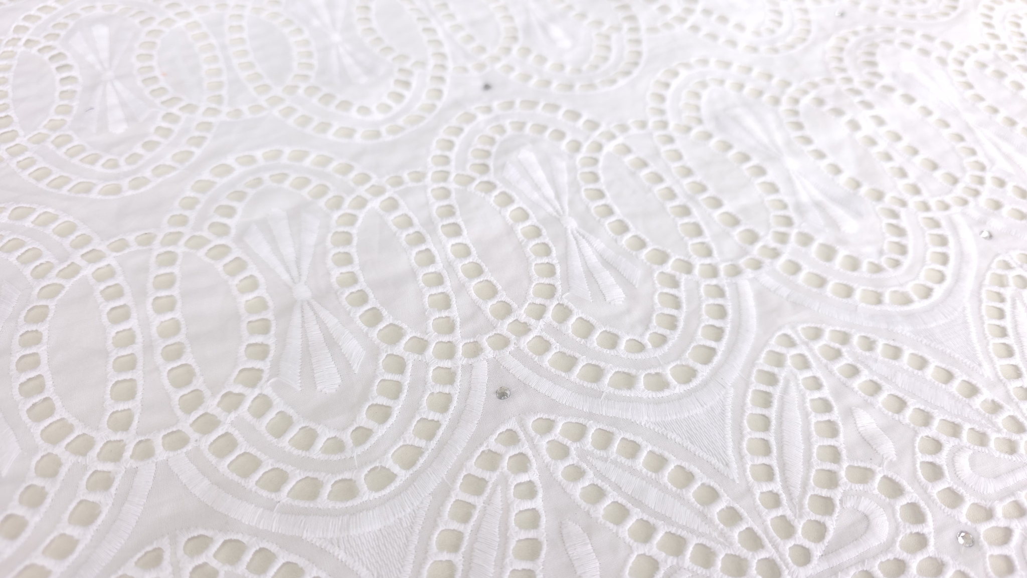 Cristal lipit pe suprafața broderiei albe cu motive geometrice și decupaje