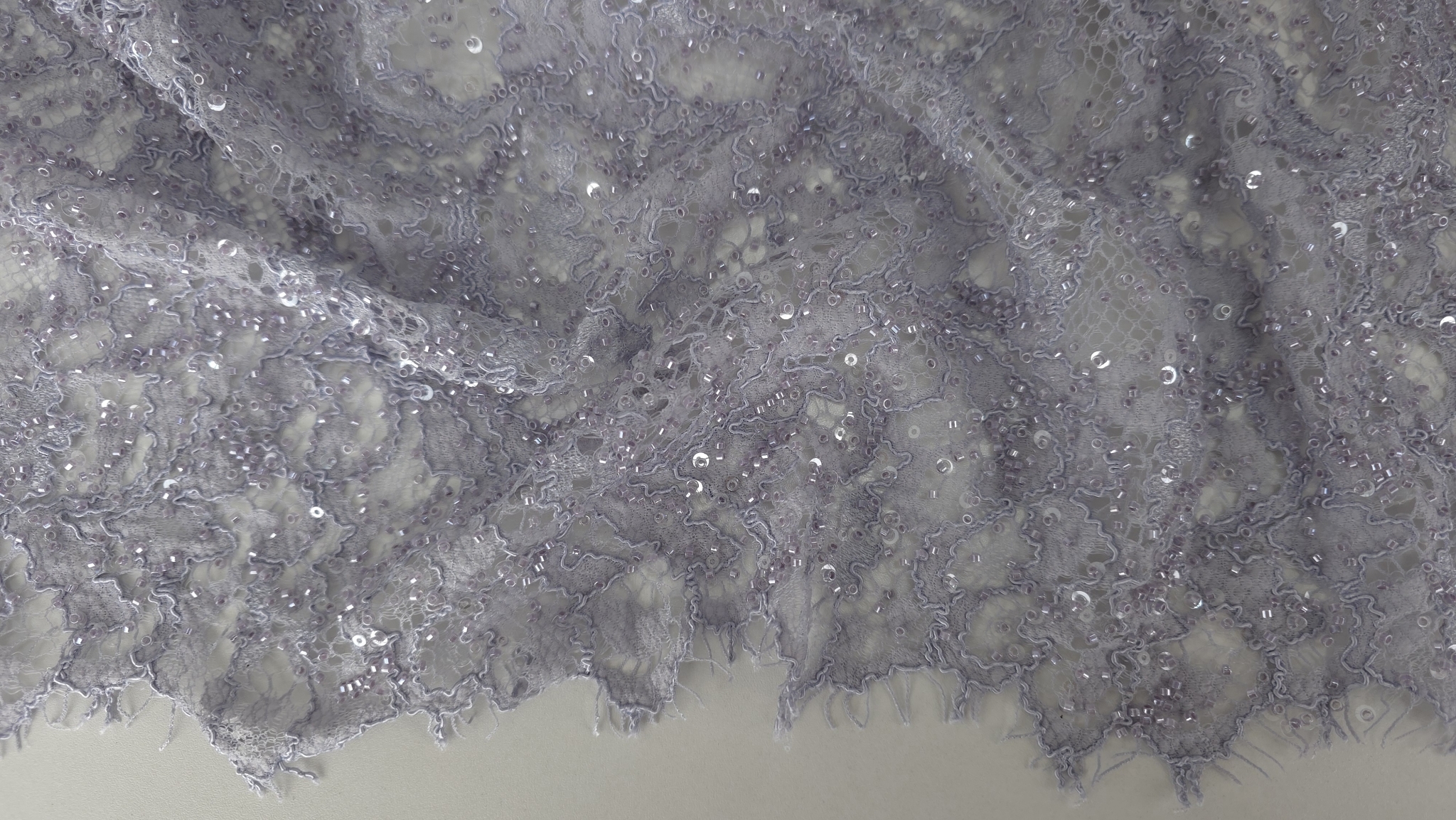 Dantelă gri lila cu mărgele pentru rochii de ocazie, material desfășurat pe suprafață plană