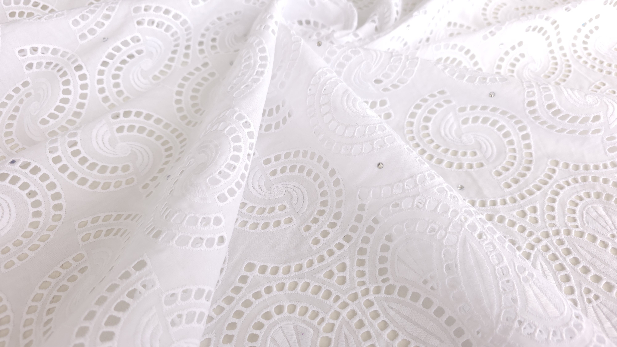 Dantelă albă brodată cu cristale lipite, vedere apropiată a spiralelor brodate și a zonelor deschise