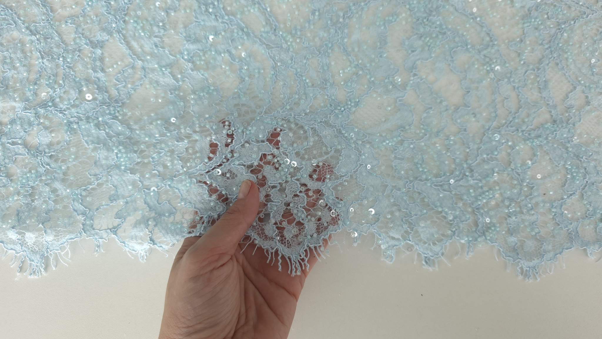 Dantelă albastru pastel cu micropaiete, detaliu pe mână arătând bordura și transparența