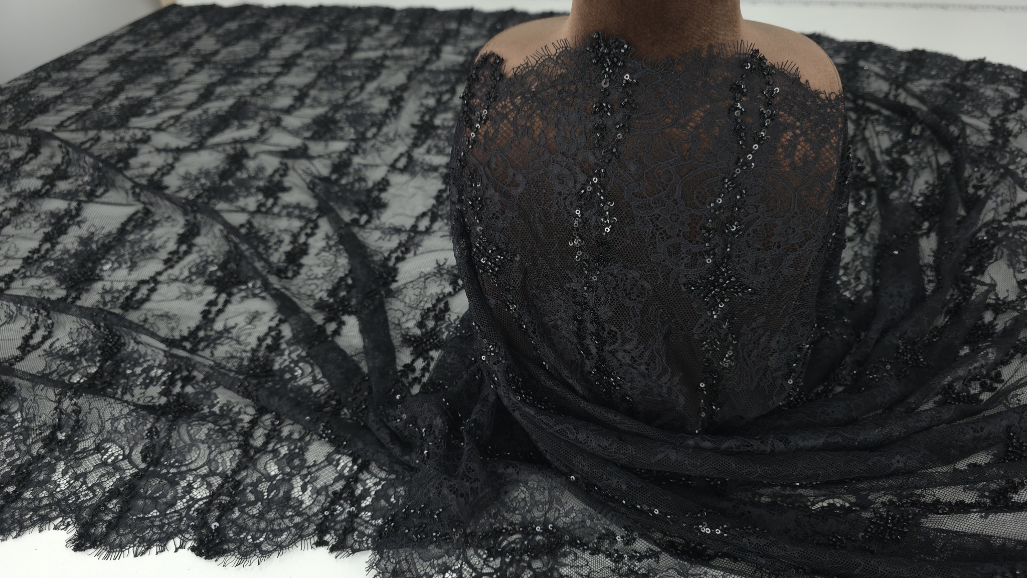Dantelă chantilly neagră drapată pe bust manechin cu micropaiete vizibile pe contururile florale