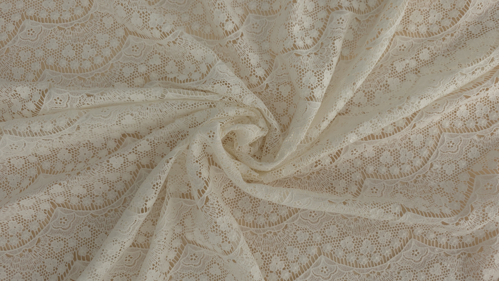 Dantela macrame ivory rasucita in spirala pe masa, arcade florale si textura retelei vizibile