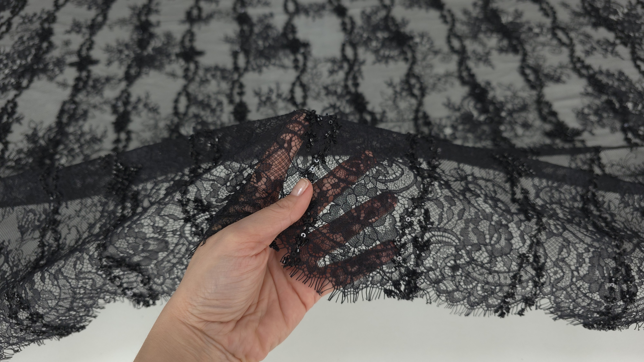 Dantelă neagră cu micropaiete ținută în mână pentru evidențierea transparenței tului