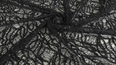 Dantelă neagră rebrodată cu margele și paiete prezentată pe suprafață albă cu falduri centrale