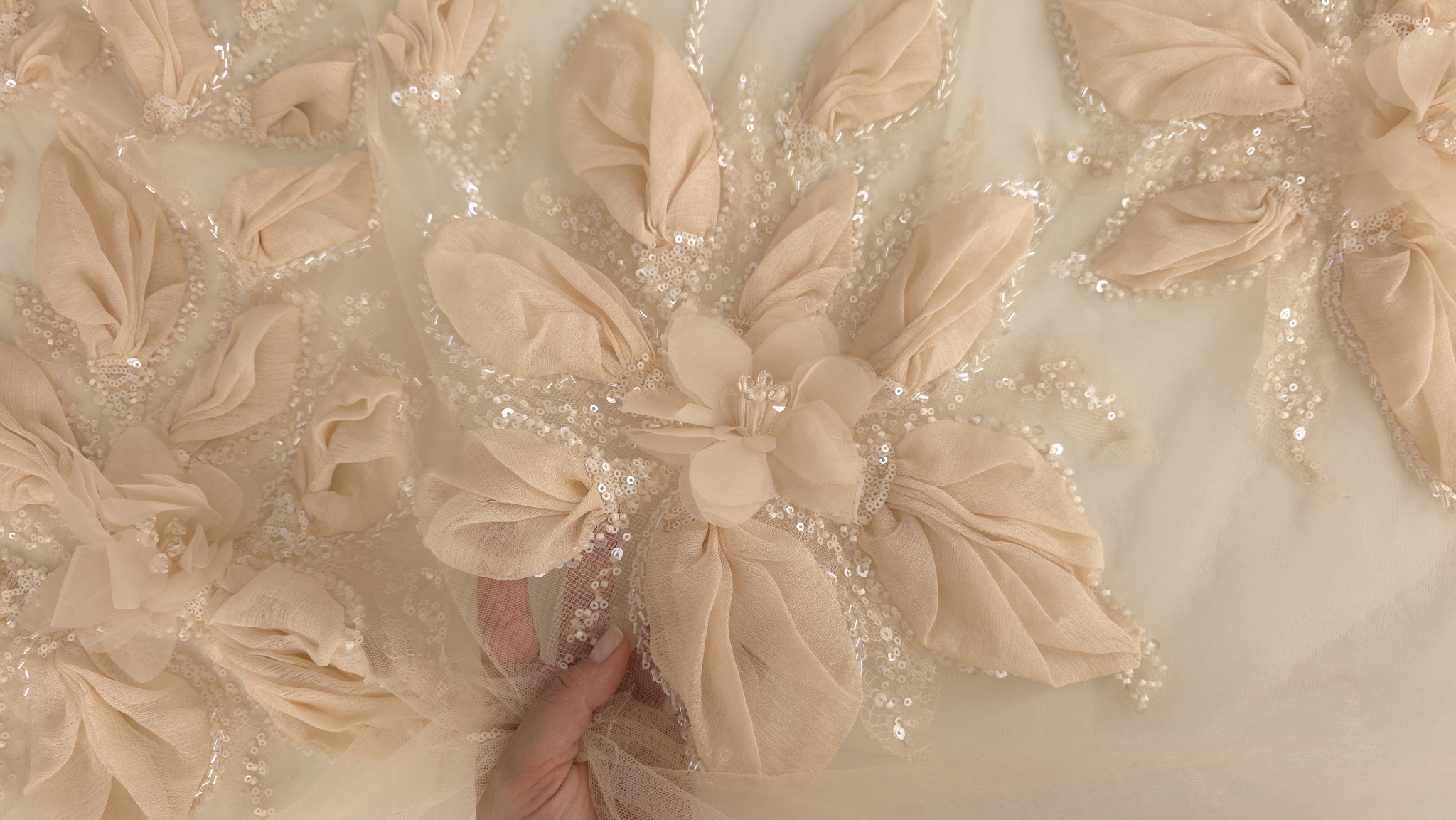 Dantelă peach brodată 3D ținută în mână, cu floare centrală și mărgele cristaline vizibile în detaliu