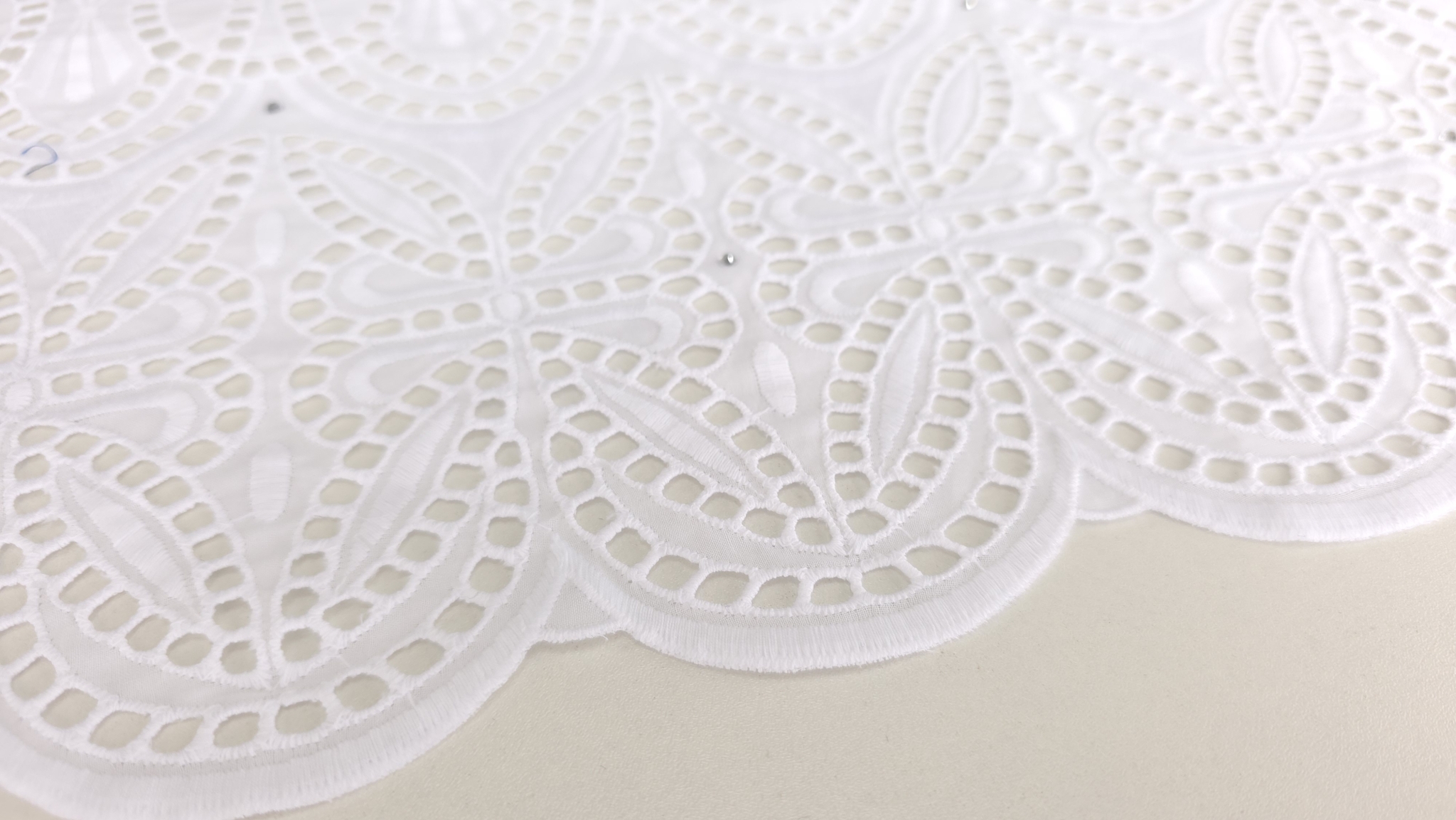 Dantelă perforată albă cu aplicații de cristale, ridicată de mână pe fond contrastant