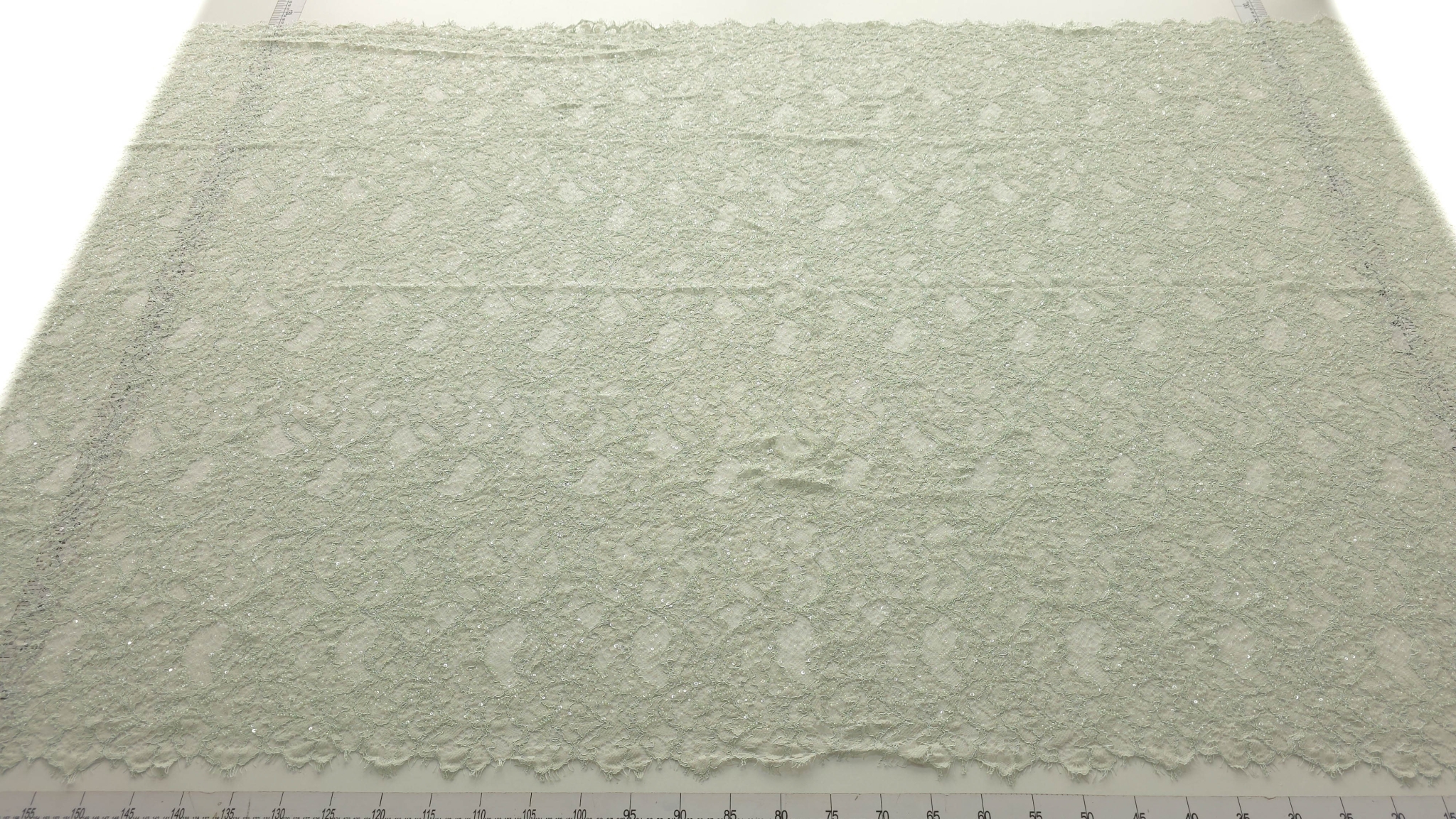 Dantelă verde pastel accesorizată cu mărgele și paiete, vedere de ansamblu pe masa de croit