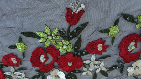 Model floral detaliat pe broderie metraj cu margele si pietre, incluzand flori rosii, crem si mici flori albastre