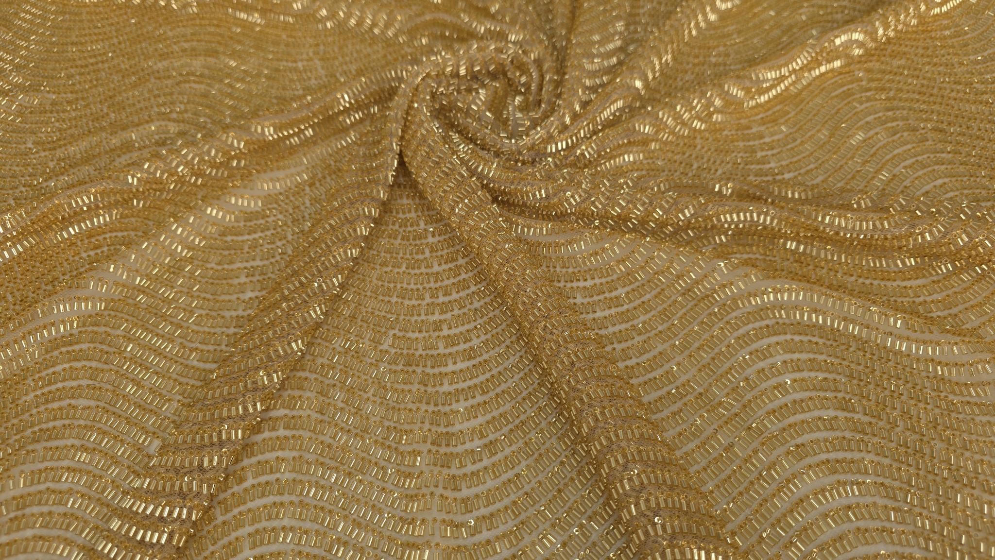 Detaliu macro pe rânduri ondulate de mărgele tubulare aurii cusute pe tul transparent