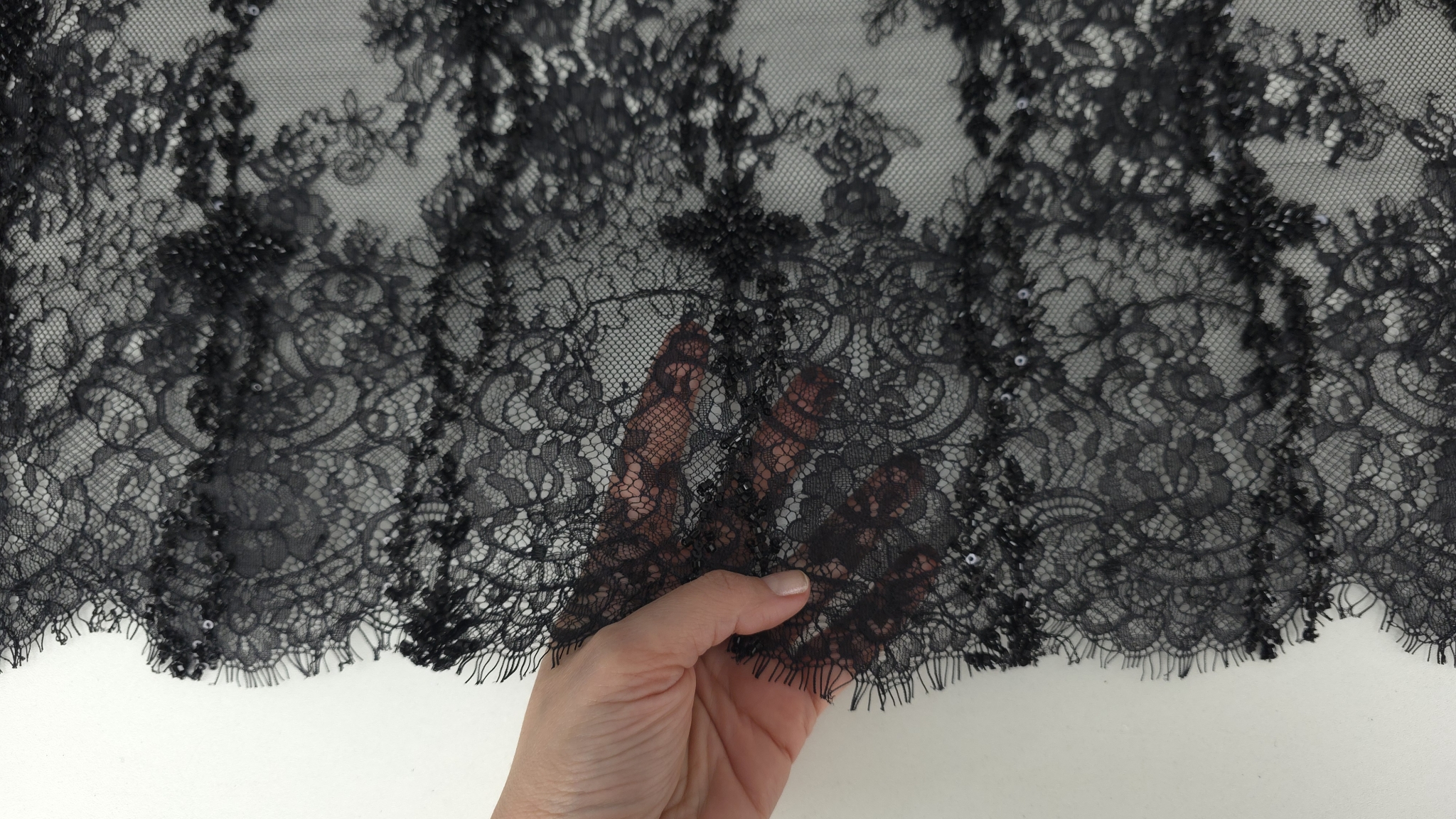 Detaliu model floral repetitiv pe dantelă chantilly neagră accesorizată cu mărgele fine