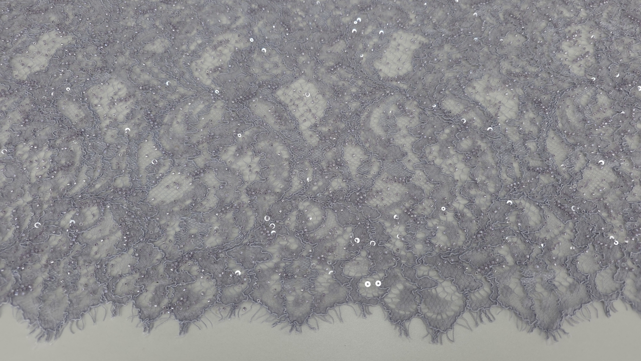 Detaliu plan apropiat pe broderie florală cu aplicații lucioase pe tul deschis