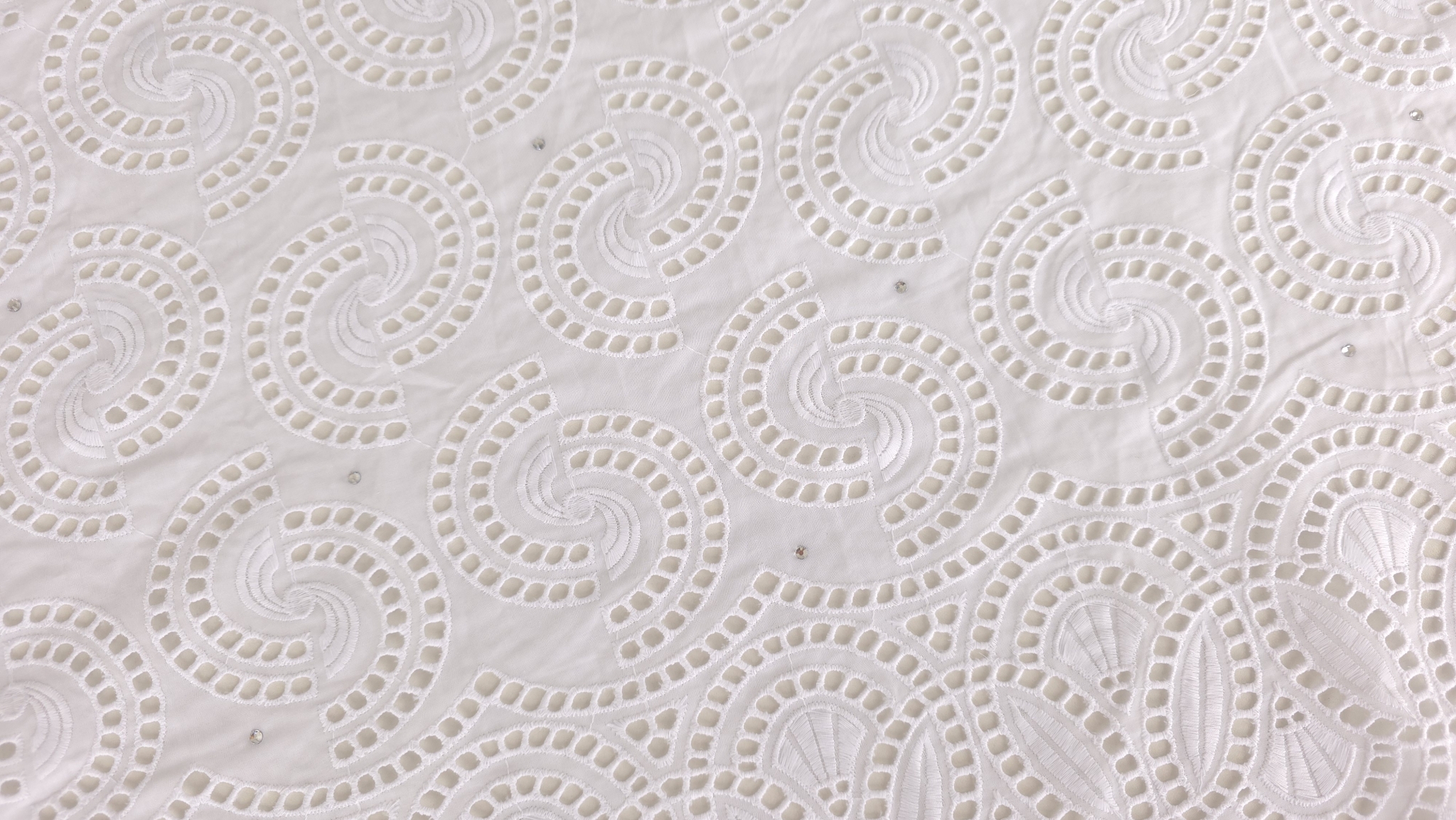 Falduri ample ale dantelei albe brodate cu spirale în relief și cristale mici lipite