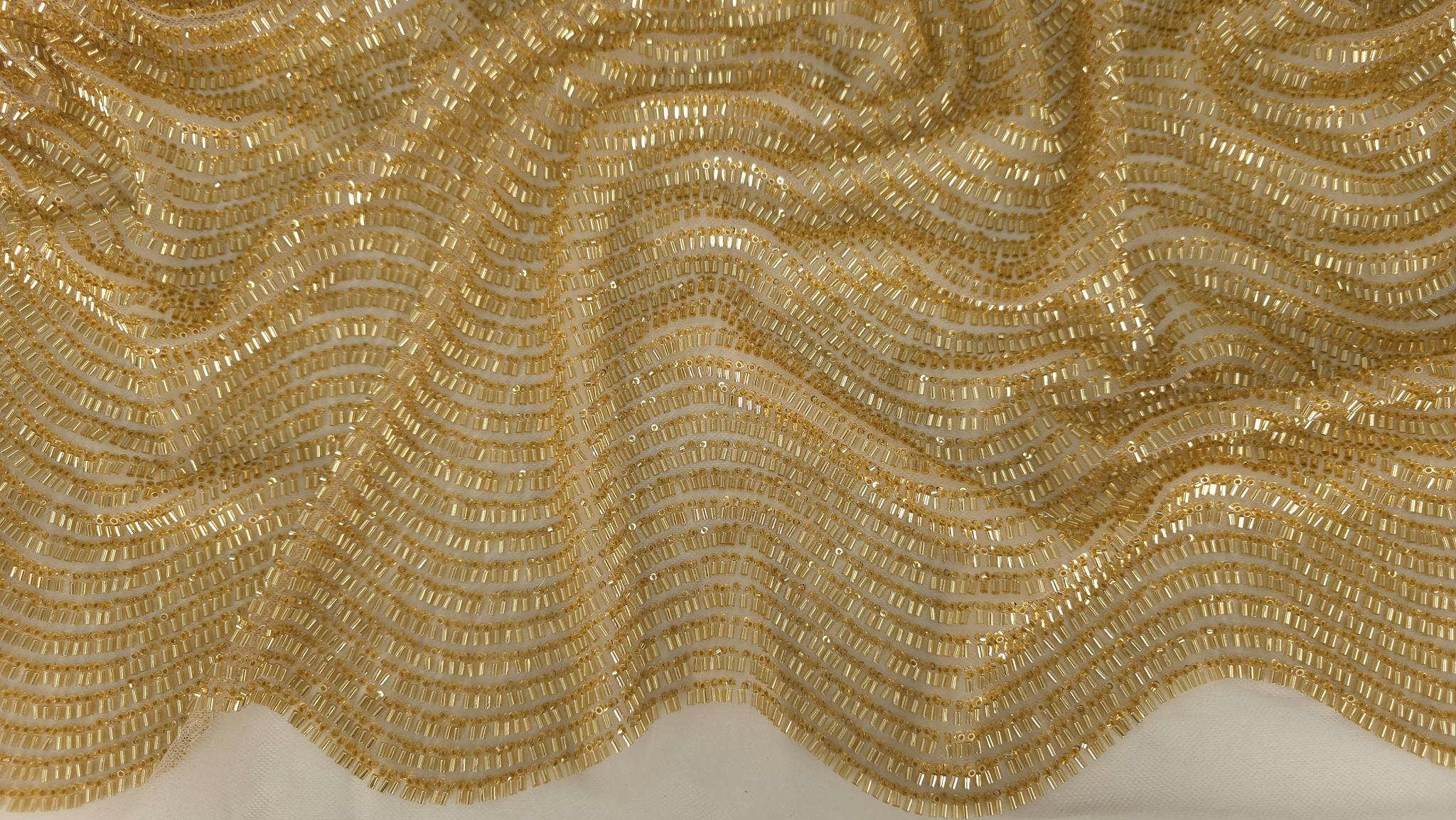 Falduri ample pe material auriu cu reflexii metalice intense și tul vizibil