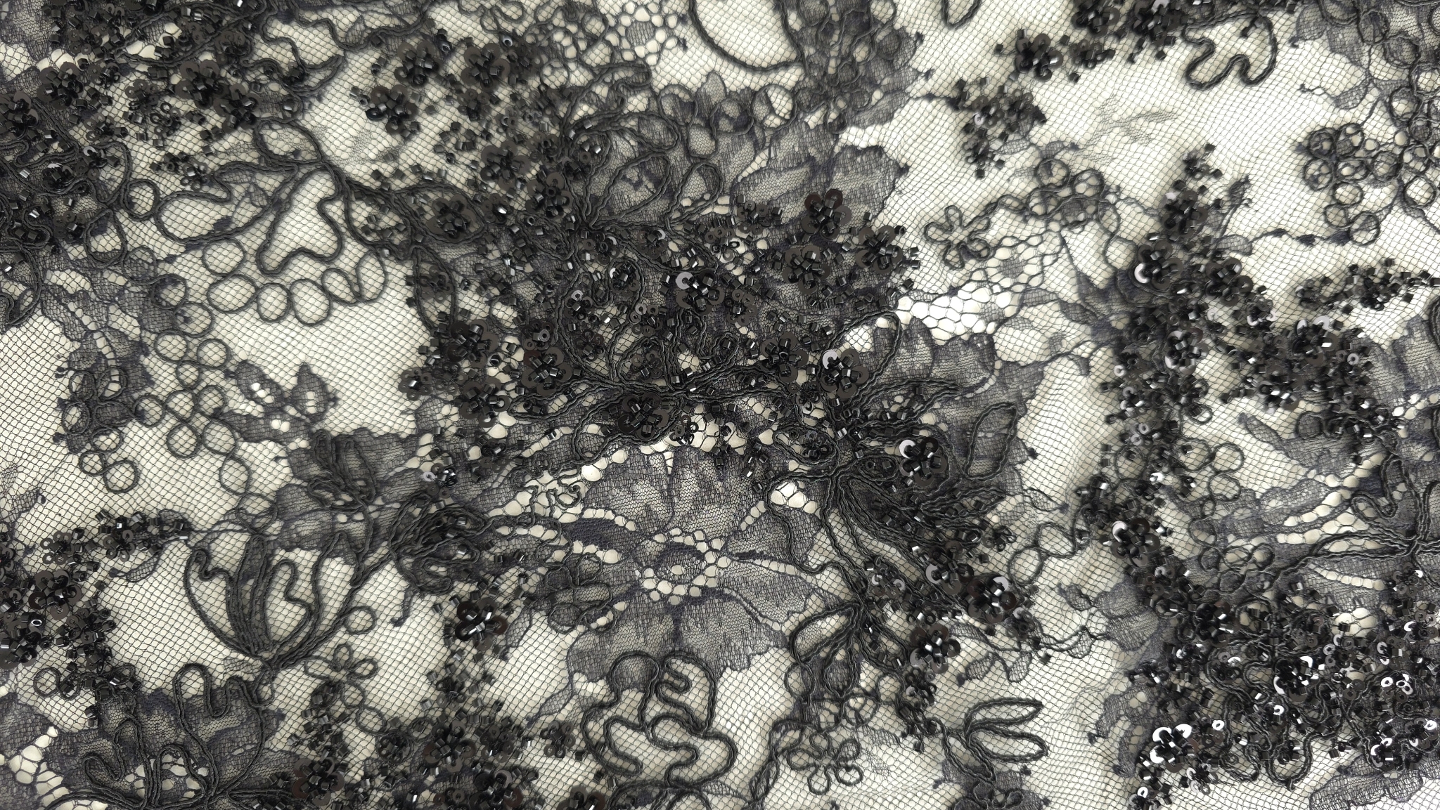 Falduri de dantelă neagră rebrodare cu reflexii de paiete pe marginea materialului