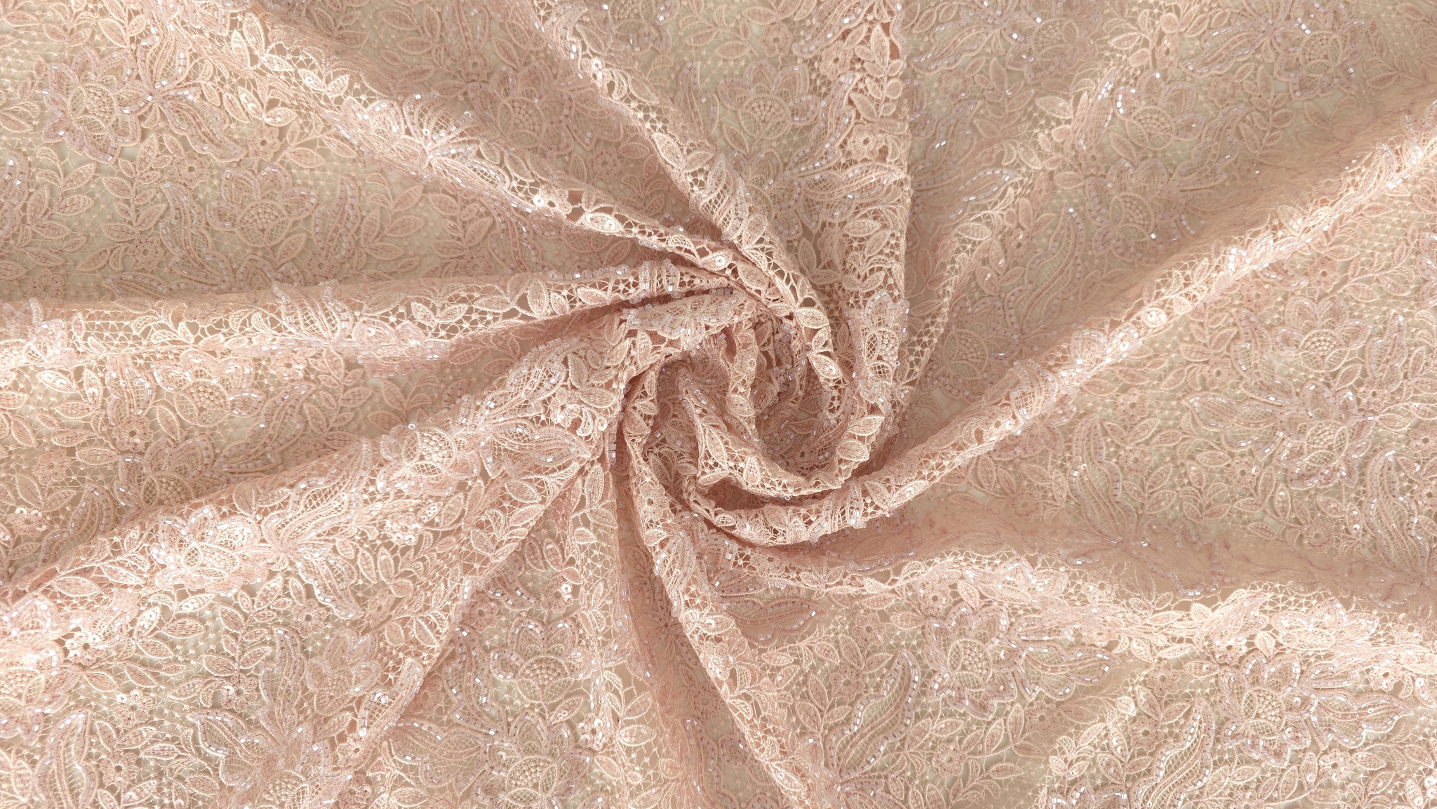 Falduri de material brodat roz pastel strânse în spirală cu motive florale dense și puncte de strălucire vizibile pe suprafață