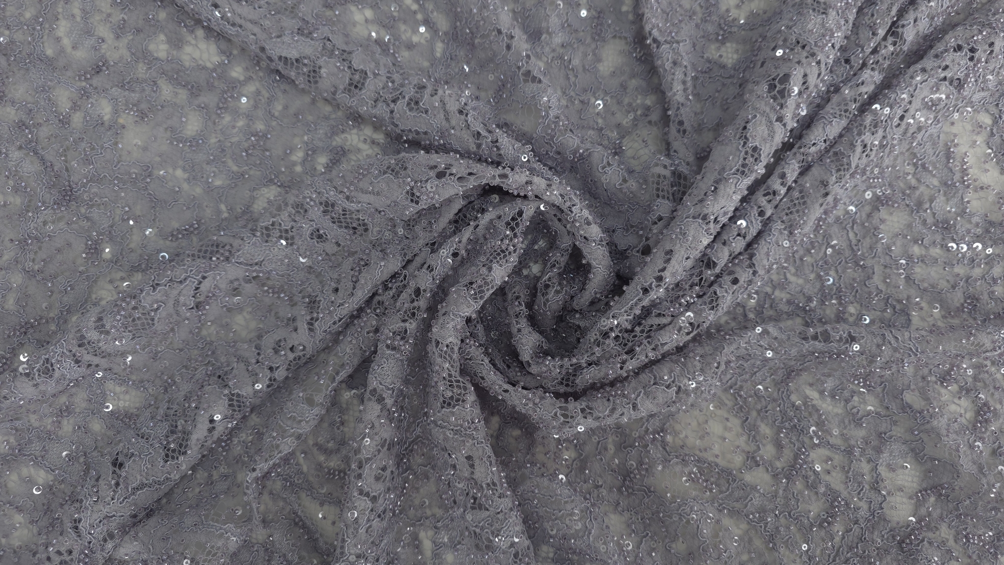 Falduri răsucite în spirală pe material textil cu broderie florală și reflexii de aplicații lucioase