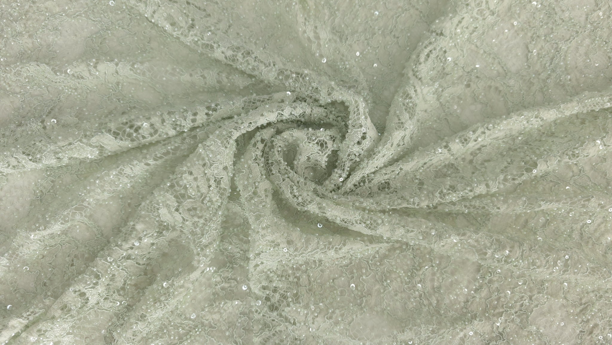 Falduri răsucite în spirală pe material verde pastel cu broderie florală și străluciri fine de paiete