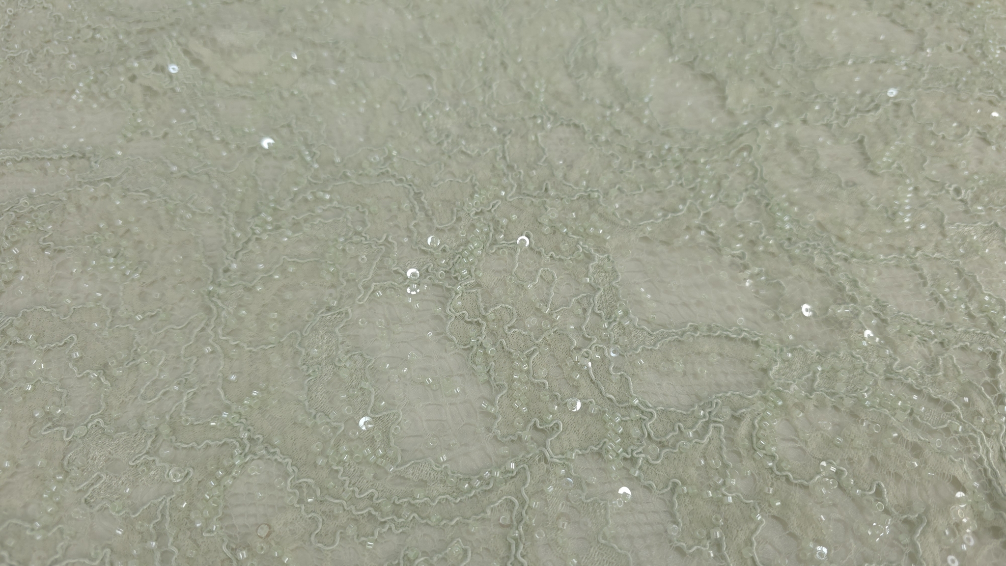 Falduri răsucite pe material verde pastel cu străluciri discrete