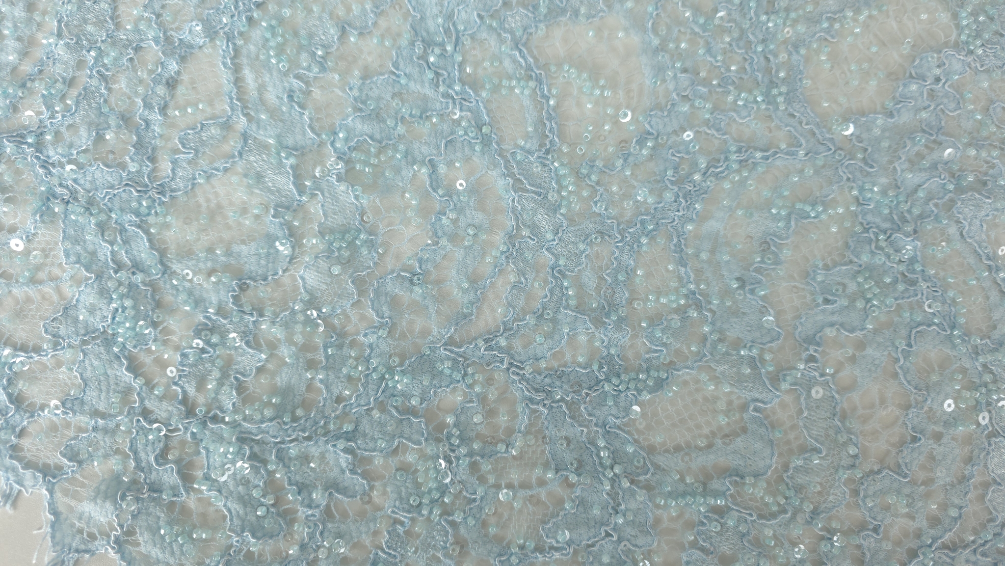 Falduri și contur scalopat pe material textil albastru deschis cu reflexii fine