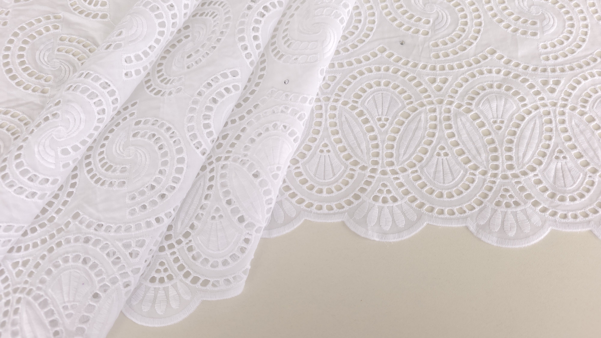 Mână ridicând bordura dantelei brodate spartă, evidențiind decupajele vizibile pe verso
