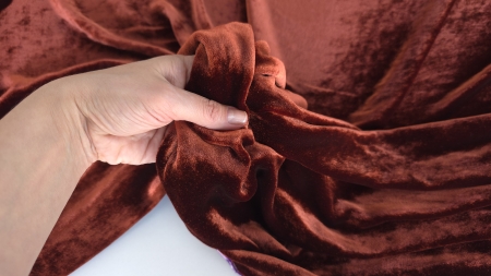 Mână ridicând colțul unui material coniac cu dosul violet vizibil parțial