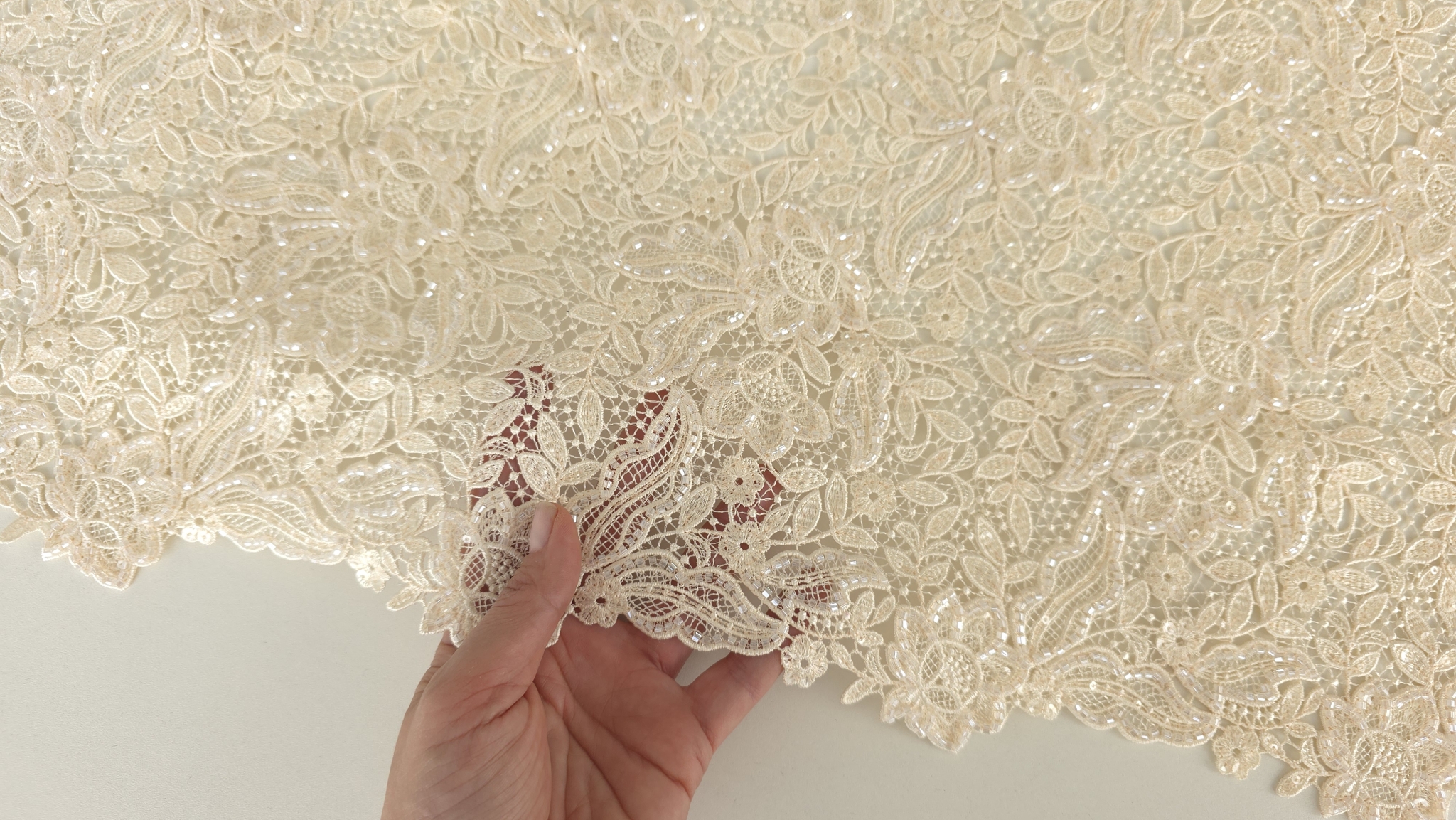 Mână ținând colțul materialului evidențiind finisajul scallop și transparența