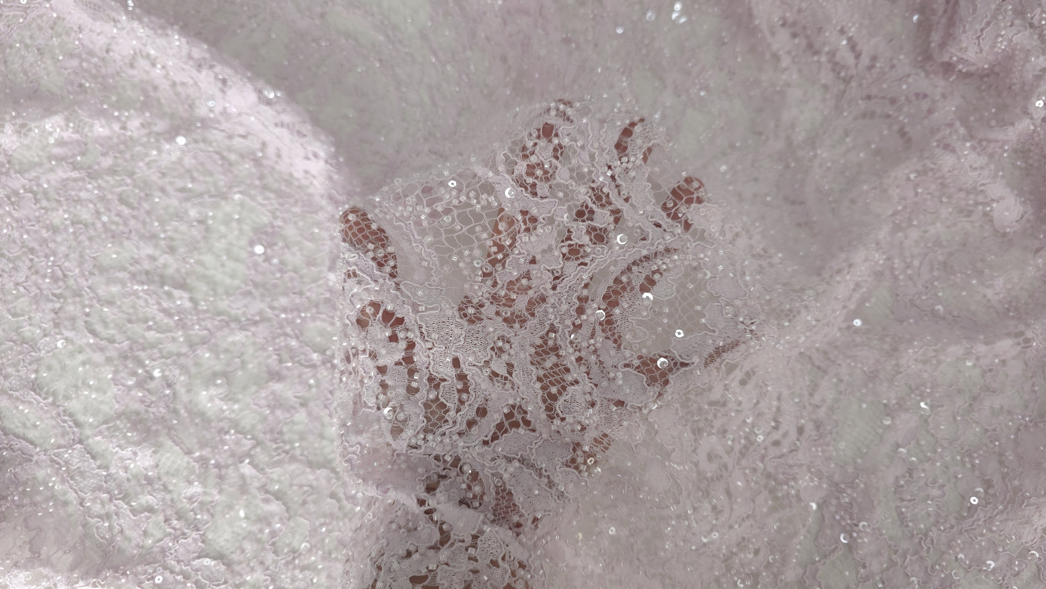 Mână ținând materialul strâns ușor, cu reflexii vizibile printre falduri