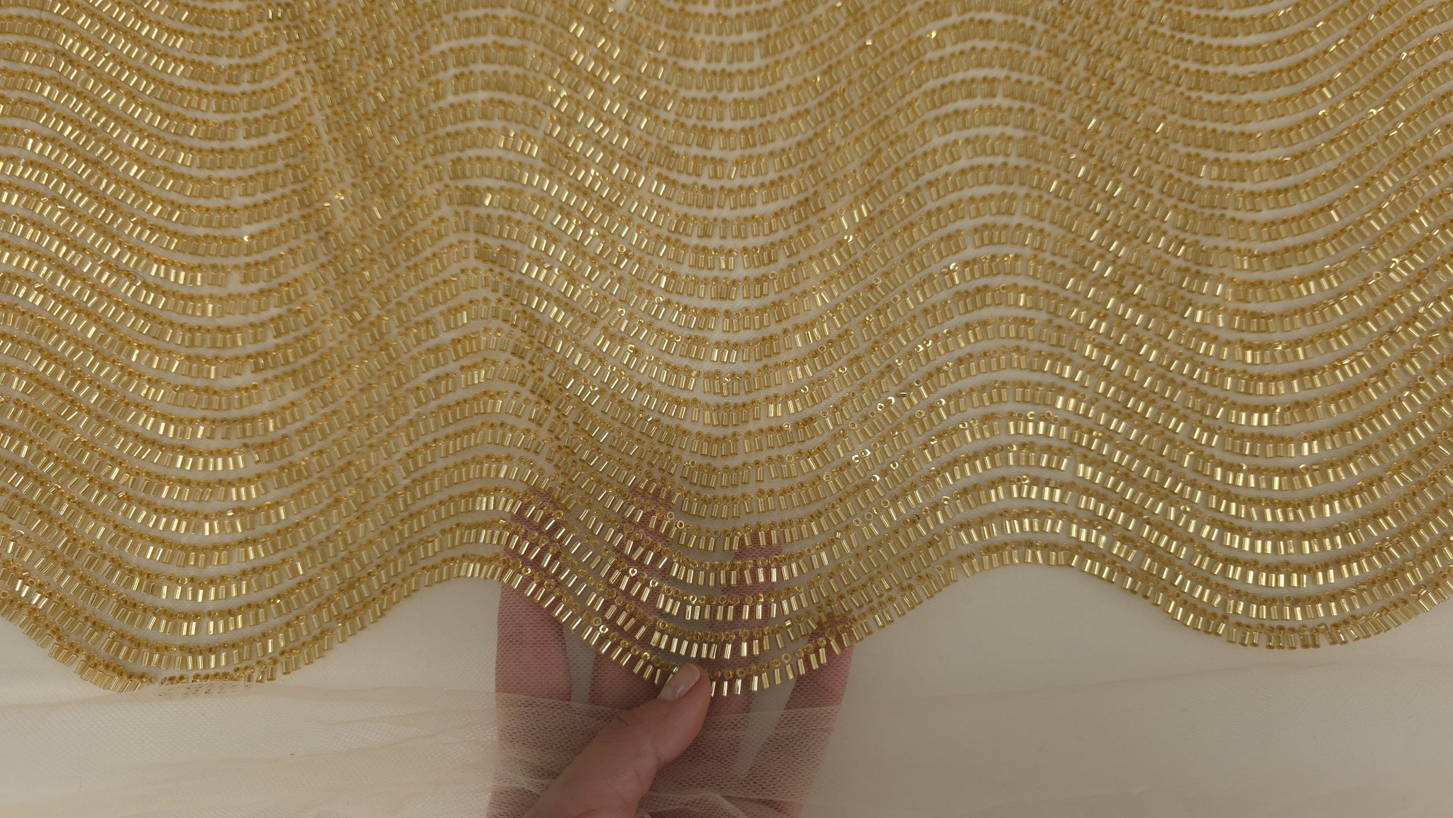 Mână ținând marginea materialului pentru evidențierea tului transparent și a cusăturii individuale