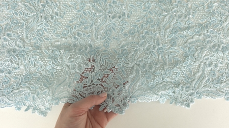 Mână ținând materialul brodat pentru a evidenția bordura și densitatea motivelor