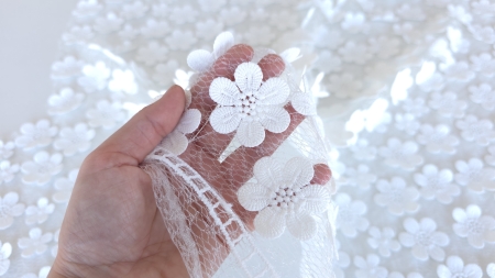 Mana tinand o dantela pe tul cu flori 3D albe pentru a observa plasa subtire si transparenta