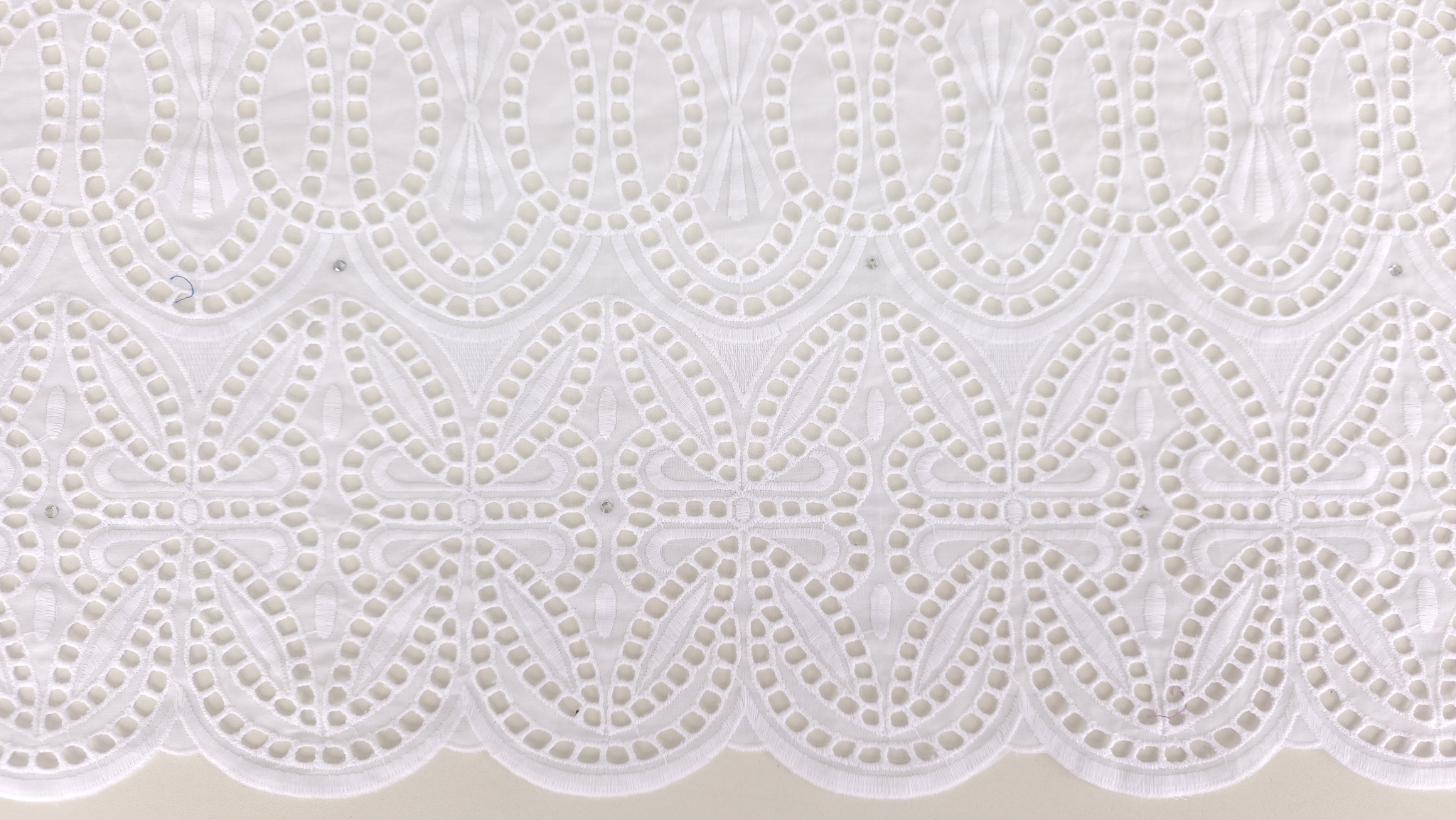 Margine ondulată cu motive geometrice brodate și perforații dense pe bumbac alb