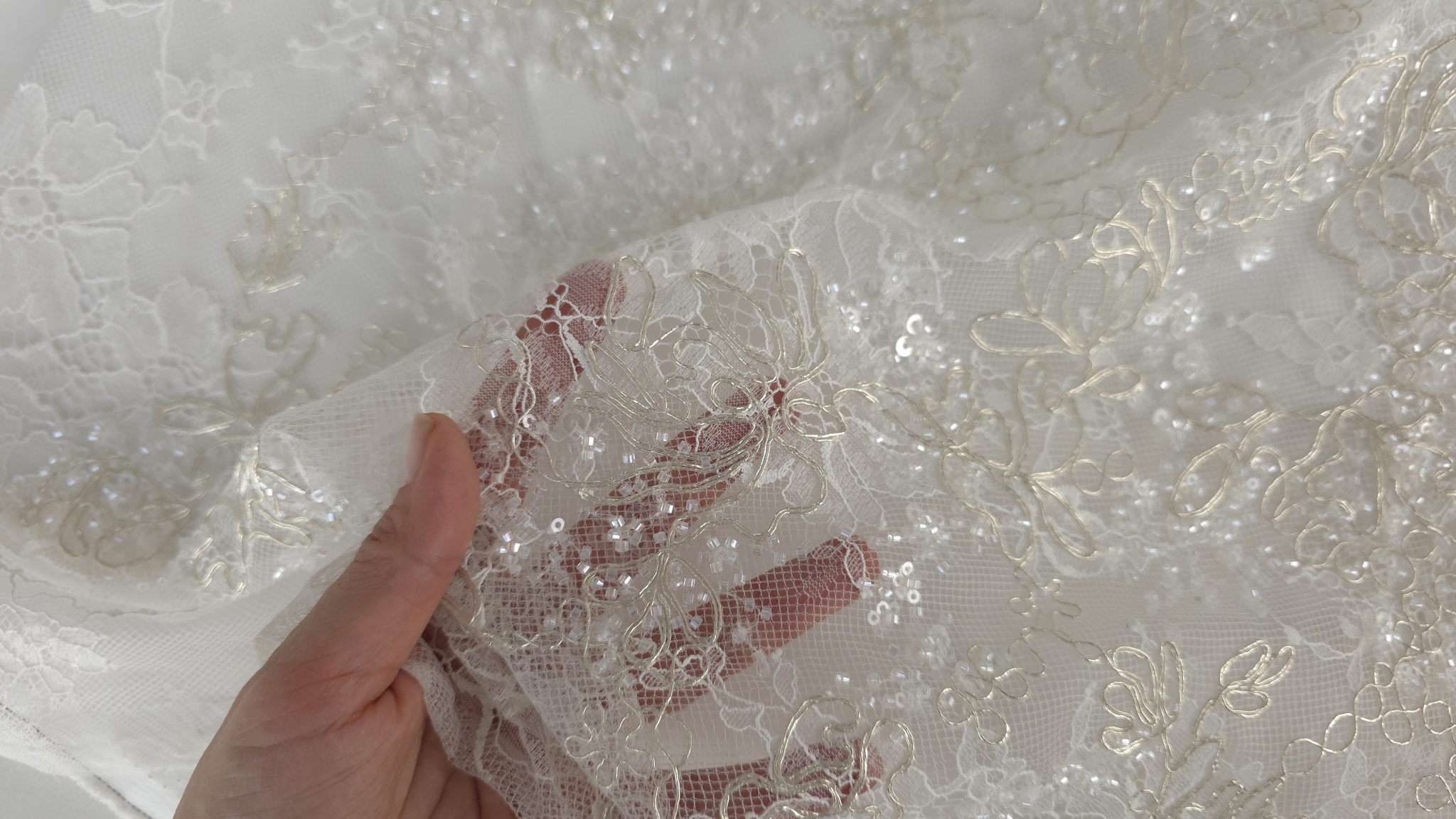 Material Chantilly cu mărgele aplicate, ținut în mână pentru a evidenția transparența