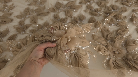 Material brodat 3D nude nisipiu ținut în mână, cu reflexii sidefate pe petale